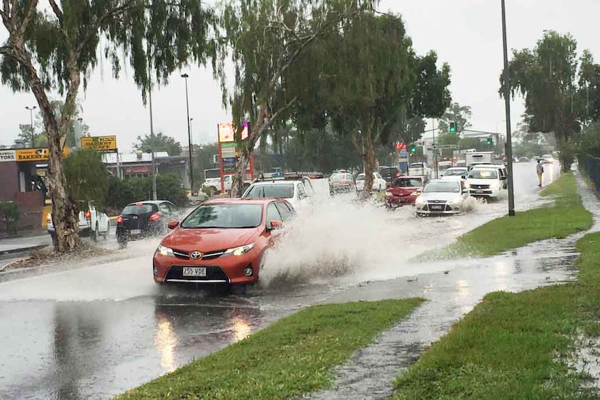 A car drives through heavy rain water at Fairfield Road in Yeronga.