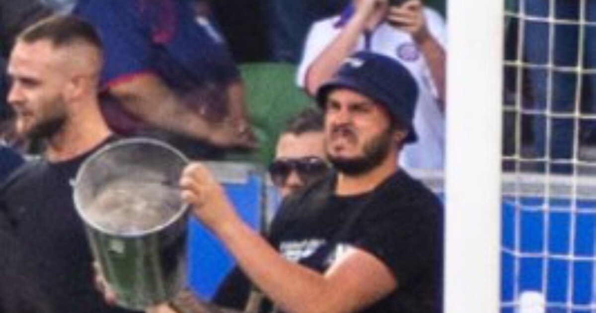 picture of a man holding a metal bucket sitting in a football stadium behind the goal post 
