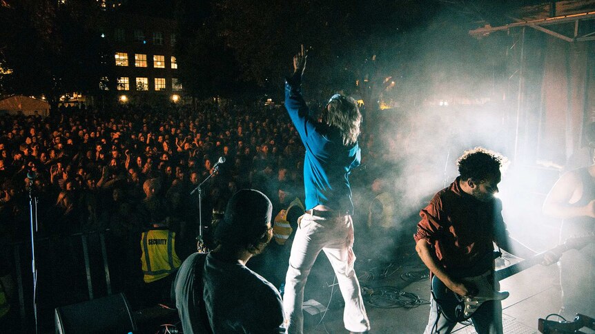 Two guitarists and a singer perform on stage to a large crowd at night time.