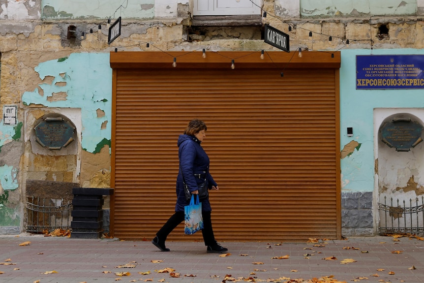 A woman walks past the rollerdoor of a closed store in Kherson. 