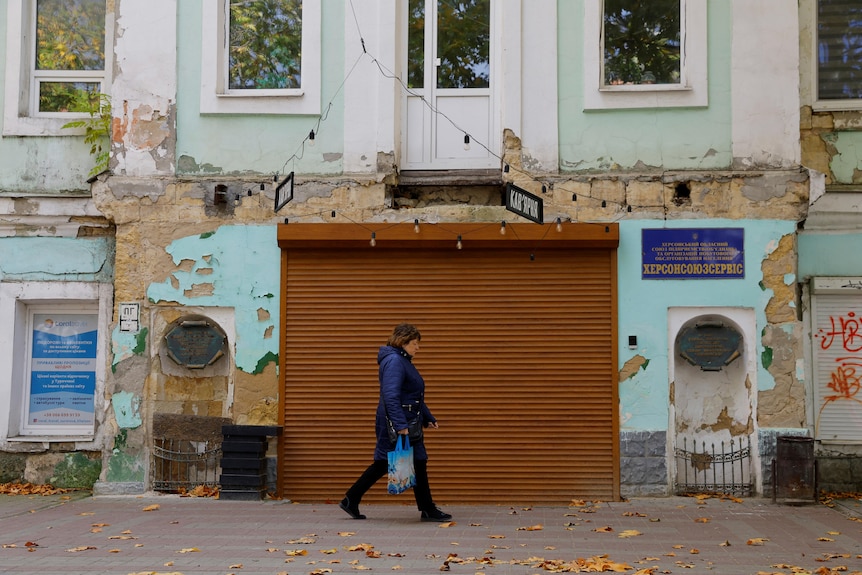 A woman walks past the rollerdoor of a closed store in Kherson. 