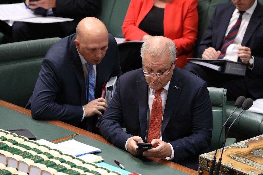 Mr Dutton and Mr Morrison are sitting in the House of Representatives, reading Mr Morrison's phone/