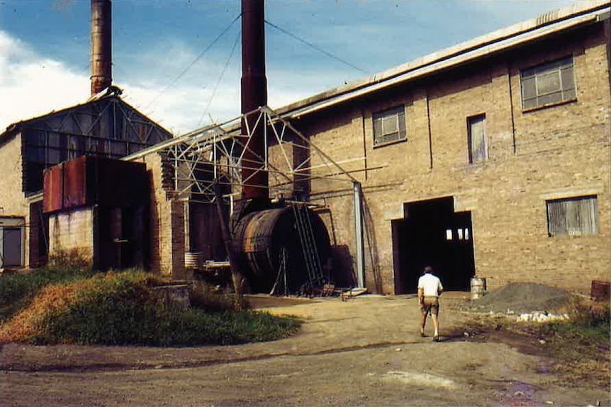 Man in white shirt and shorts walking into a brick and tin factory