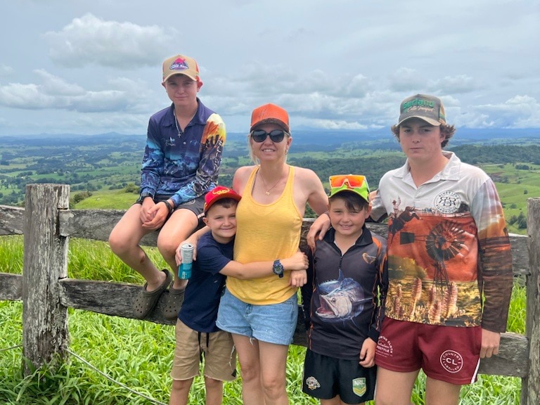 A woman and her three children pose in front of a fence with a paddock behind them.