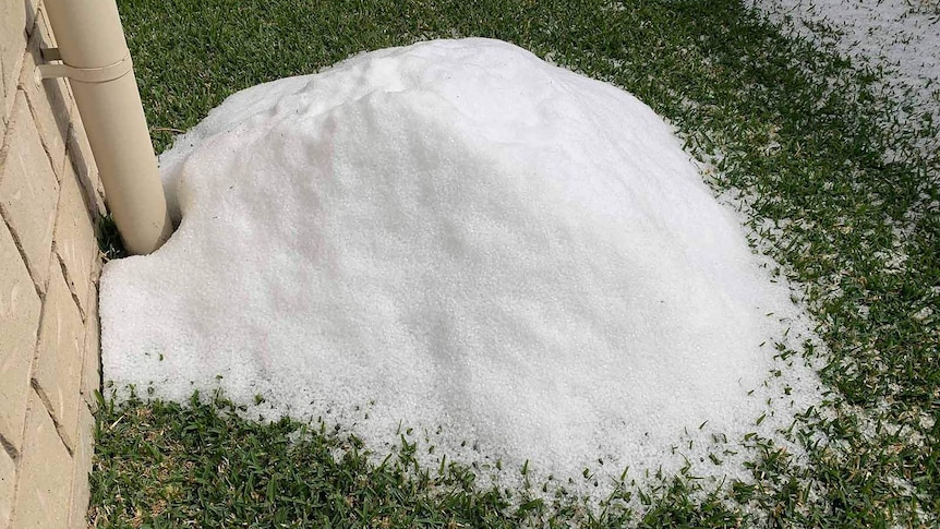 A pile of hail in the yard of a house next to a down pipe