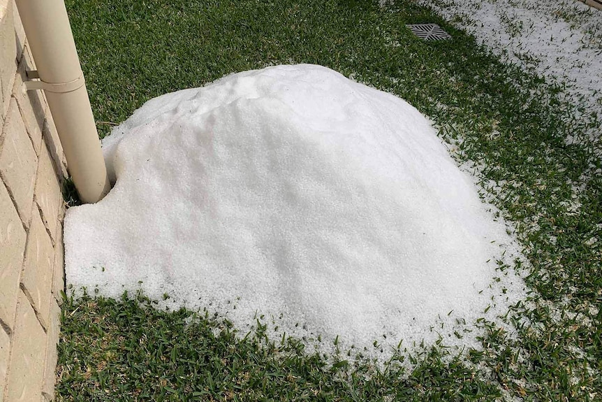 A pile of hail in the yard of a house next to a down pipe