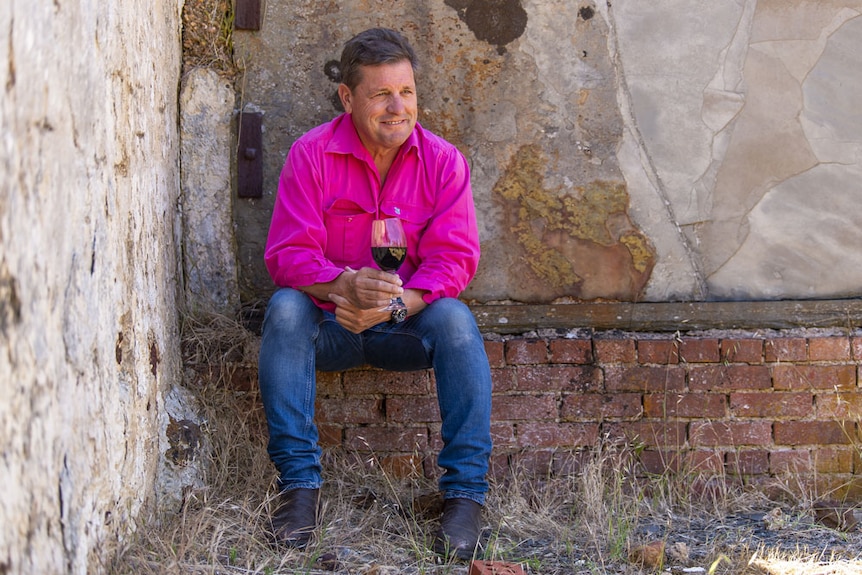 Andrew Hardy sits against a cement wall with a glass of red wine
