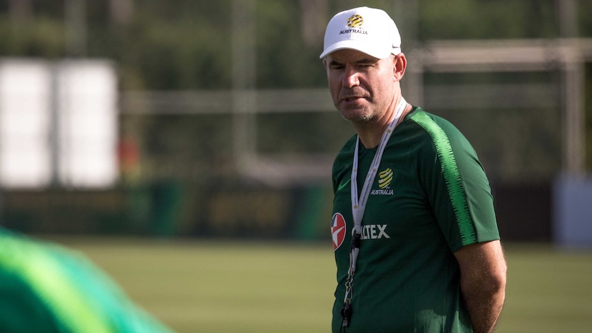 A coach in a cap stands at Socceroos training in Turkey in May 2018.