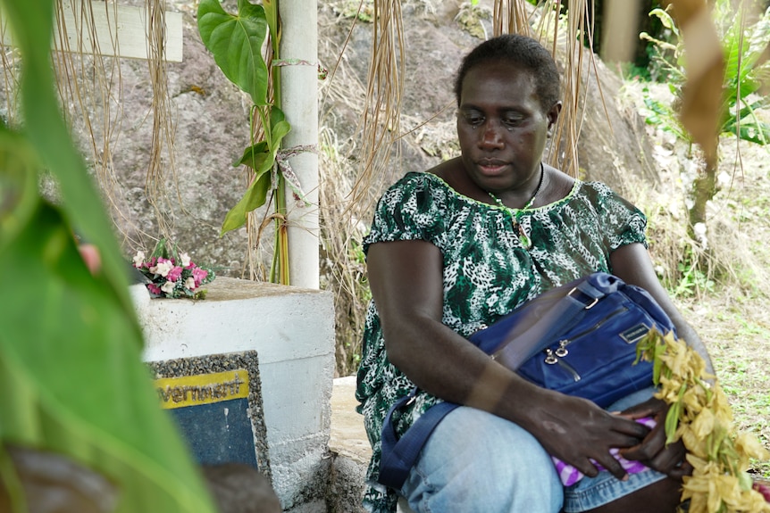 A woman holds back tears while looking at a grave.