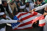A group of bearded men in traditional Pakistani clothing burn a US flag.