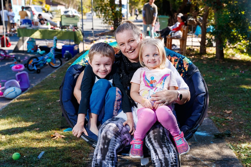 An image of Michell sitting on a chair with her two children cuddling together. 