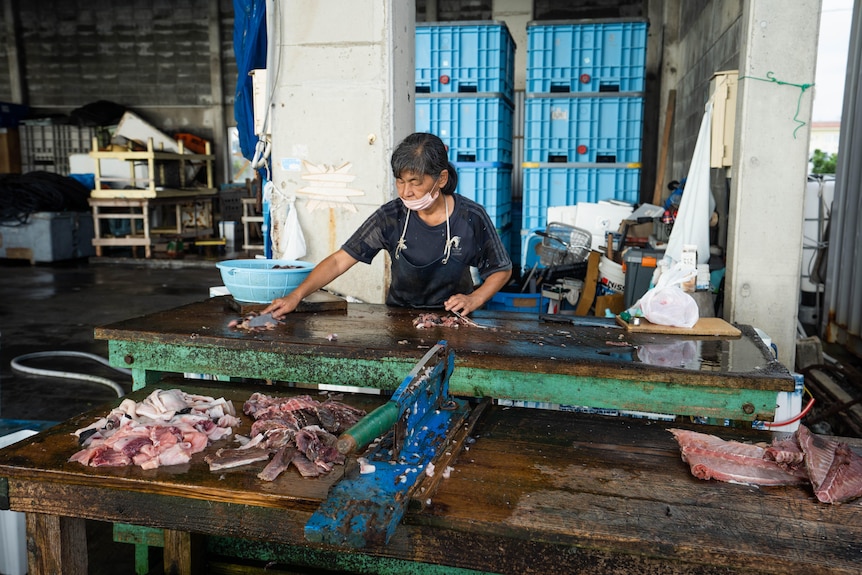 A woman with a knife cleans fish.