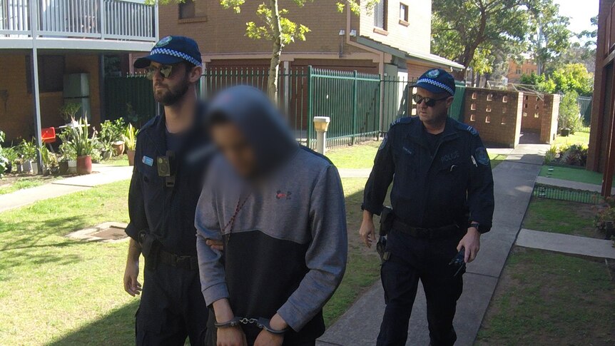 Cruz Pamoana Davis-Tuka with face blurred and handcuffs being arrested by NSW Police walking through yard
