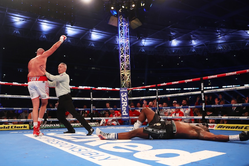 Boxer Dillian Whyte lies flat out in the ring after being knocked out as the referee pushes Tyson Fury away in the background. 