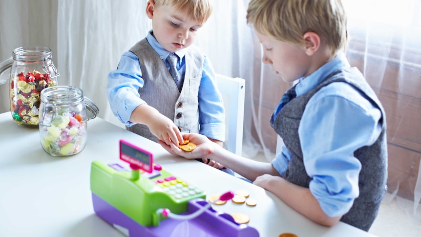 Two young boys playing with a toy cash register exchanging play money and lollies