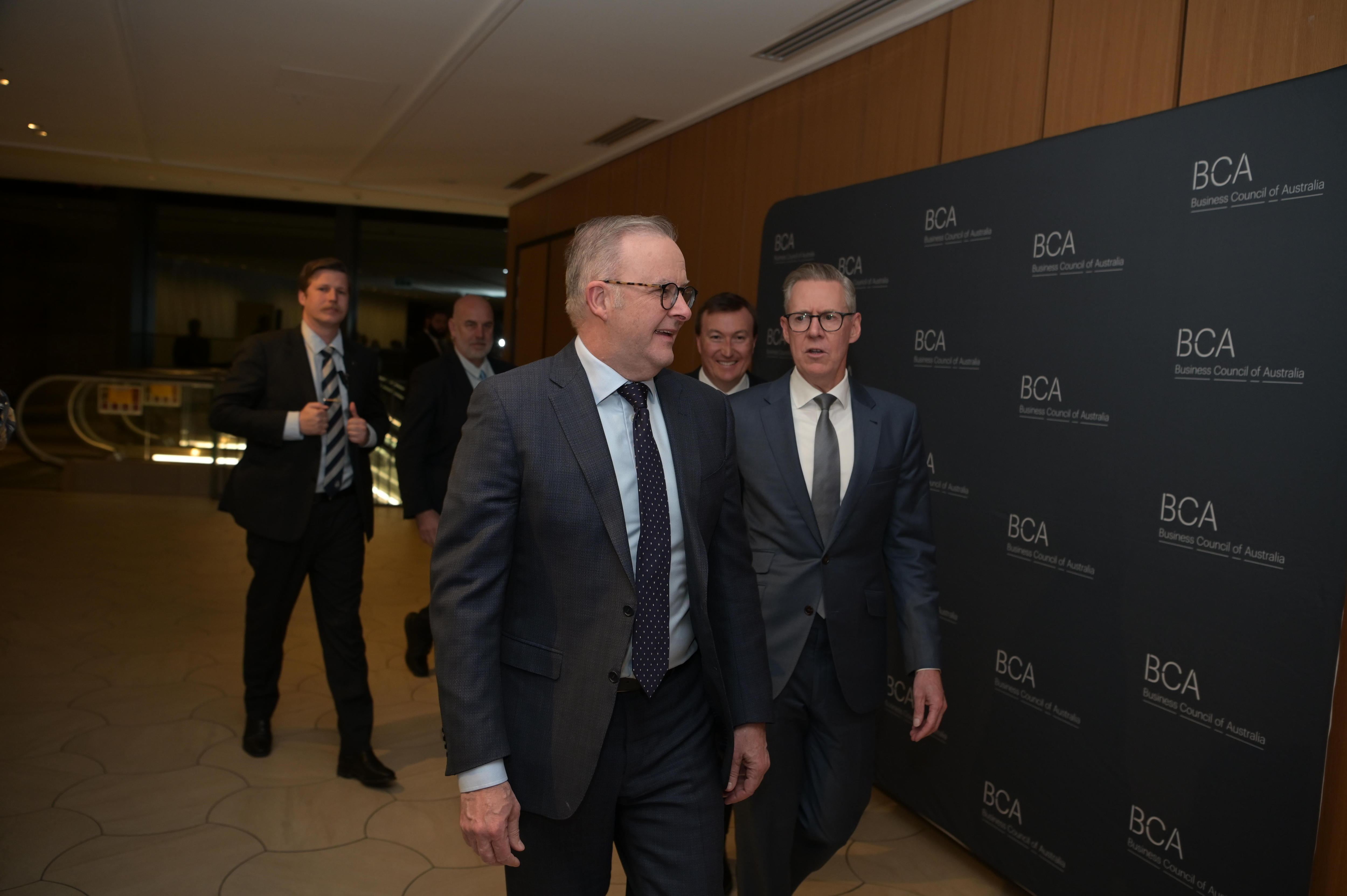 Albanese and four other men walk down a hallway, the BCA logo visible on material behind them.