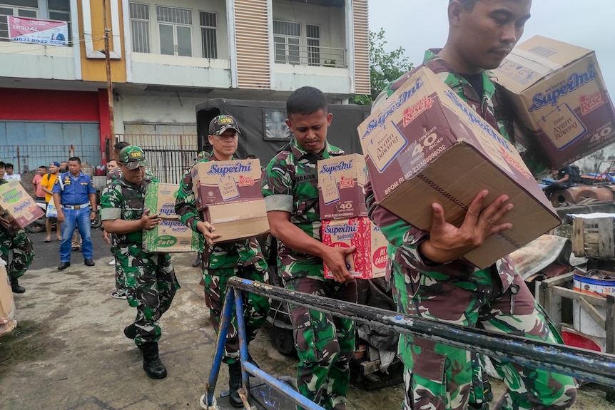 Indonesian military personnel load food items onto a ship.