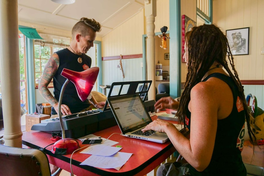 A person at a keyboard and another person sitting at their laptop typing.