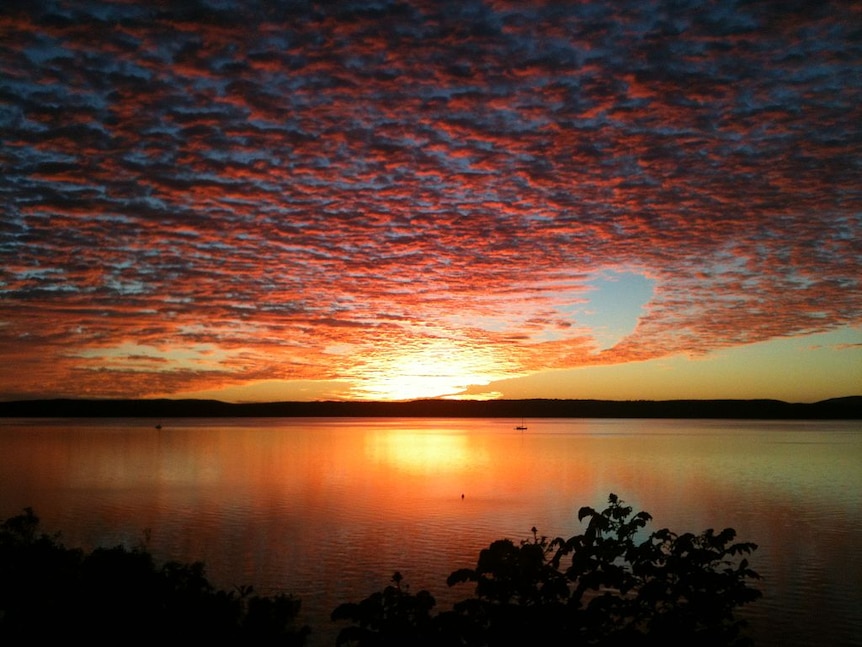 A sunrise, water, land in foreground and background.