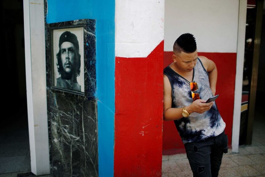 Pemuda Kuba mengecek ponselnya di hotspot internet dekat foto revolusioner Che Guevara.
