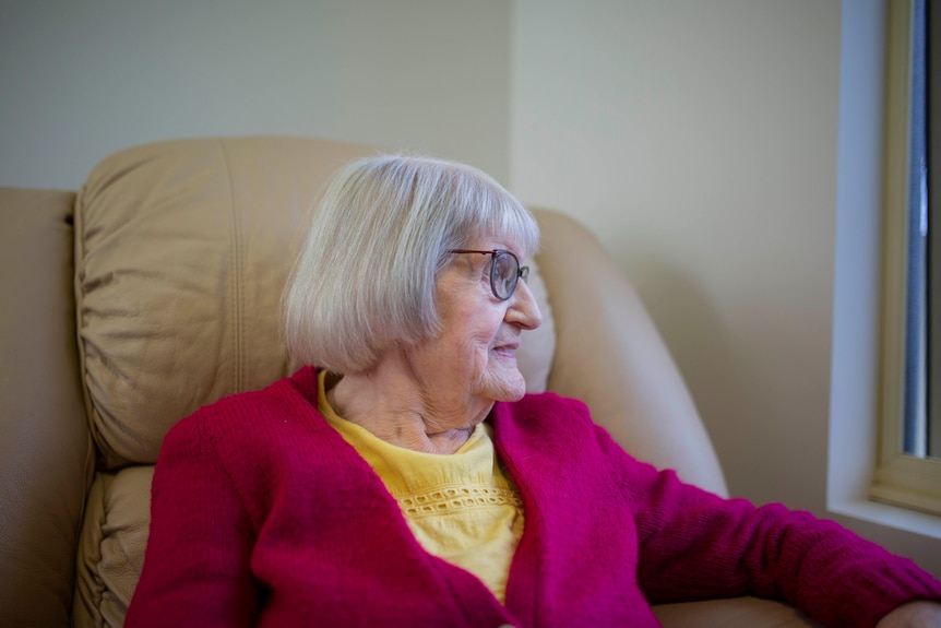 An aged care resident sits in her chair and looks out a window