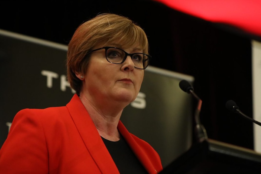 Linda Reynolds stands at a podium where she is addressing a crowd