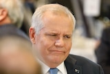 Scott Morrison grimaces as he sits at a table, with his glasses off.