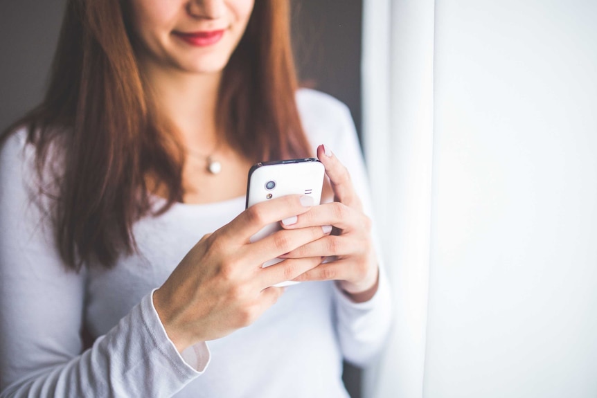 A photo of a woman wearing all white sending a text message to depict safe sexting.