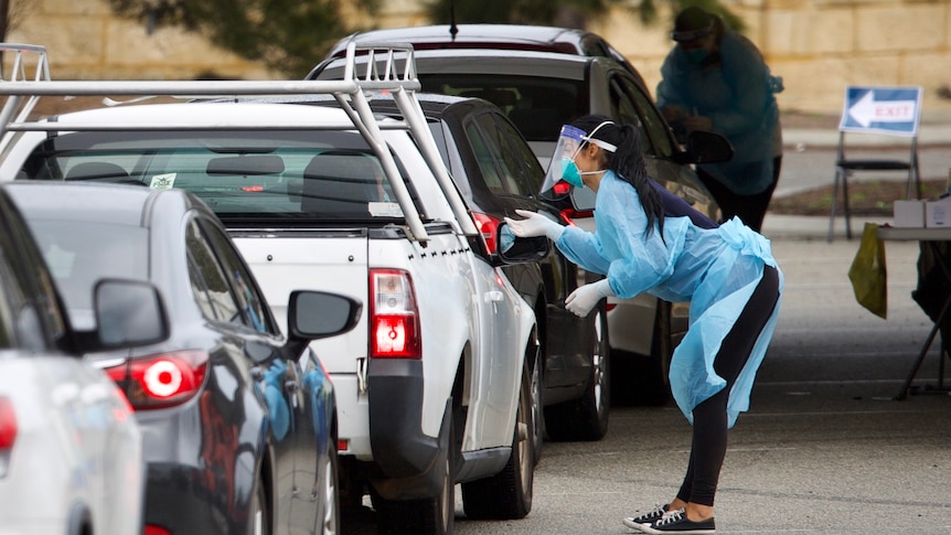 A woman tests drivers for COVID at a drive-through clinic.