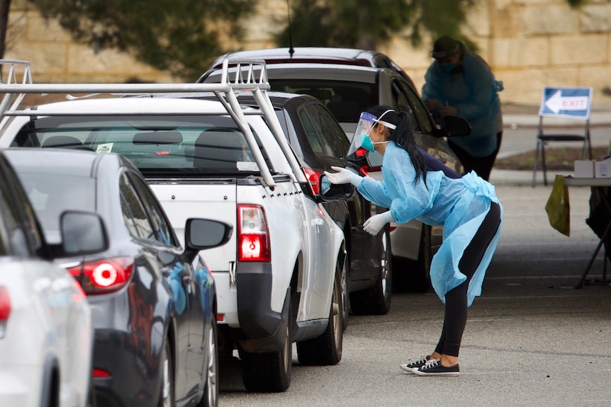 A woman tests drivers for COVID at a drive-through clinic.