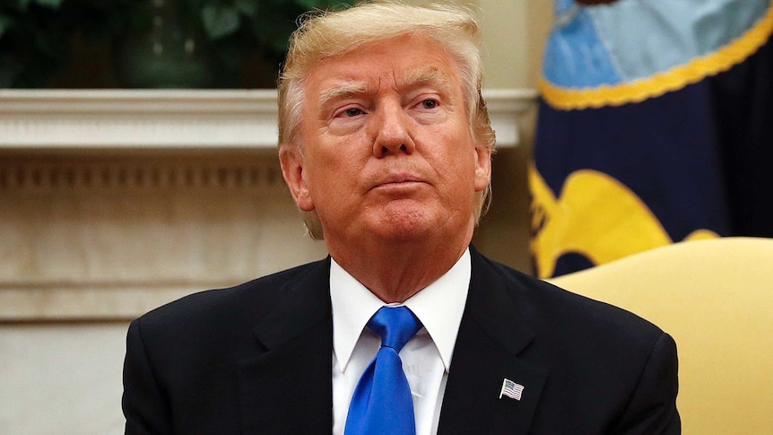 Donald Trump sits on a yellow couch in the Oval Office with a pensive expression on his face, looking to the right.