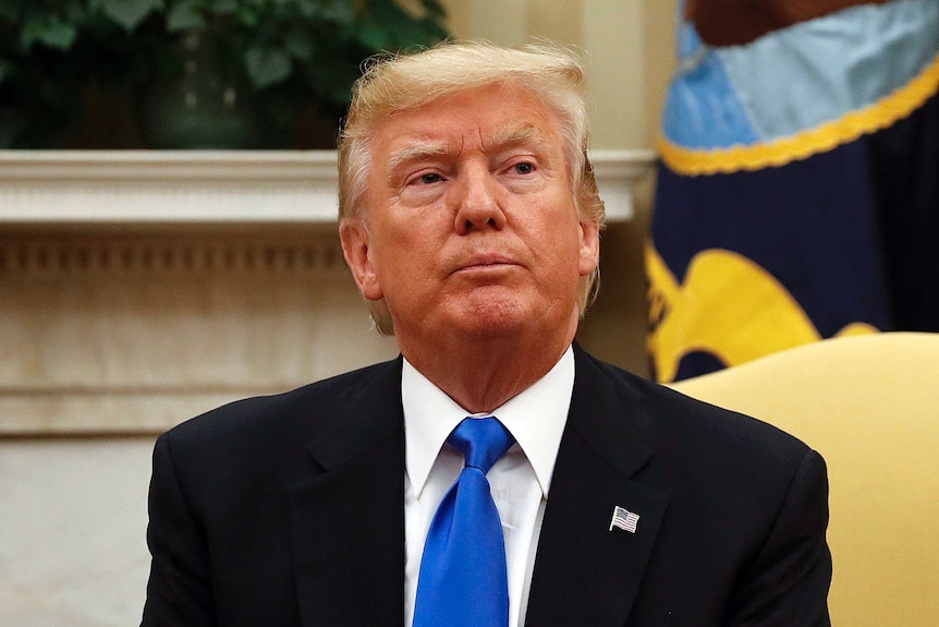 Donald Trump sits on a yellow couch in the Oval Office with a pensive expression on his face, looking to the right.