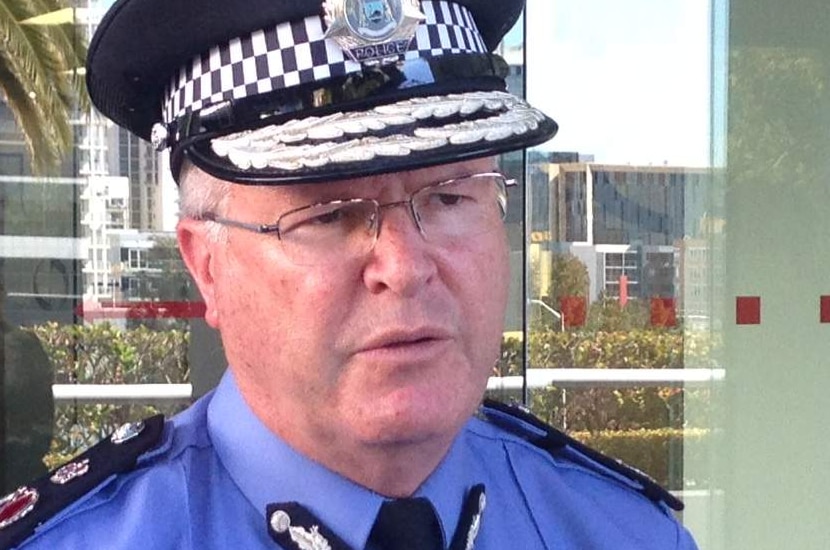 A man in police uniform talks to the media outside some glass sliding doors.