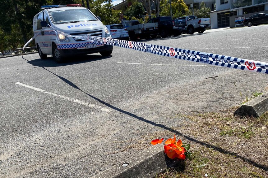 An orange flower on the side of the road next to police tape and police van on empty street.