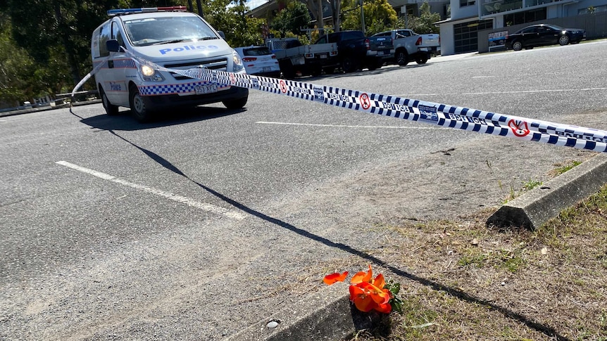 An orange flower on the side of the road next to police tape and police van on empty street.
