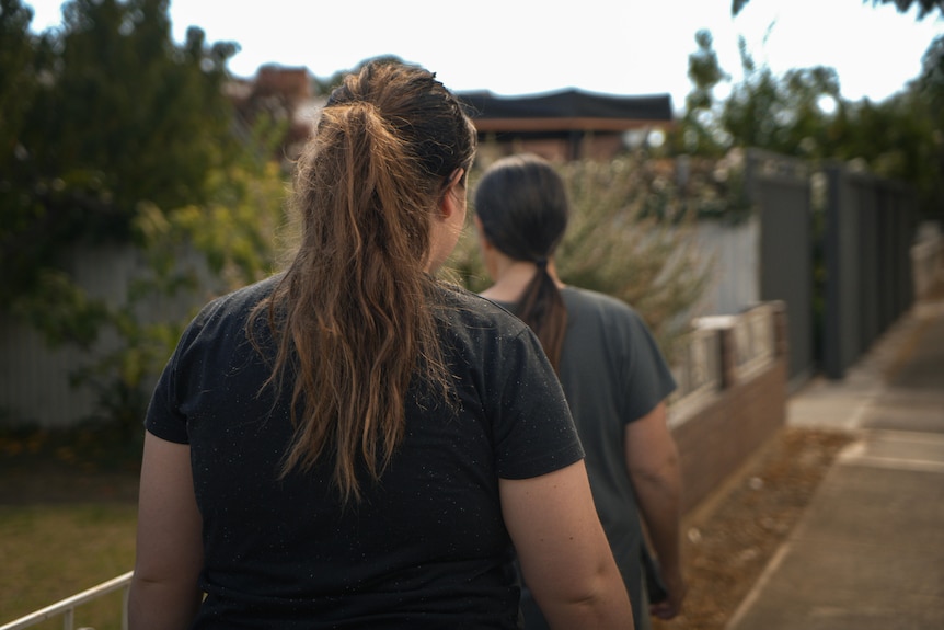 Two women in dark t-shirts with pony tails have their backs to the camera as they walk along a suburban footpath.
