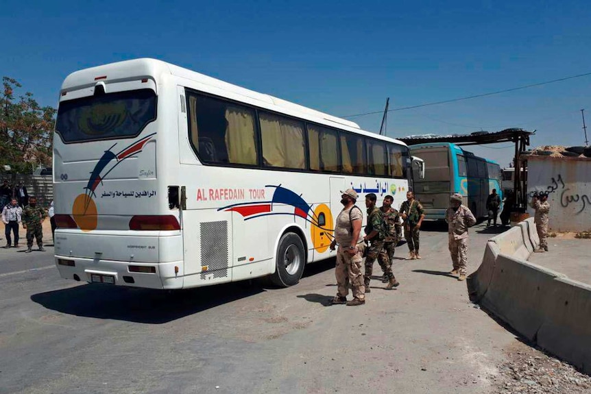 Busses are seen passing a checkpoint overseen by men in military uniforms.