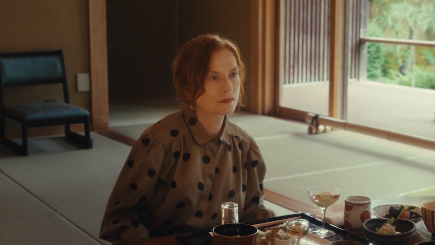 Red-haired woman in black and red dotted dress sits for a Japanese meal in traditional tatami mat room