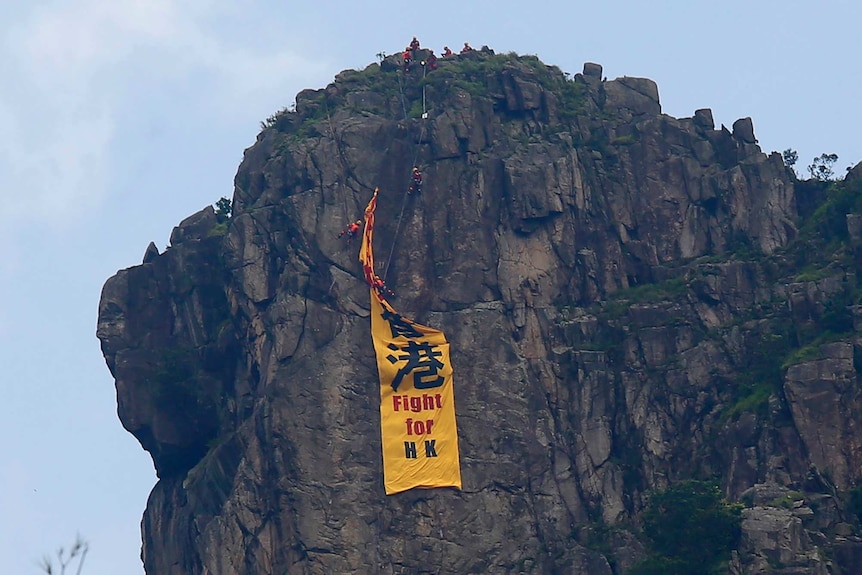 Firefighters remove a yellow banner with the words "Fight for Hong Kong" from Lion Rock mountain.