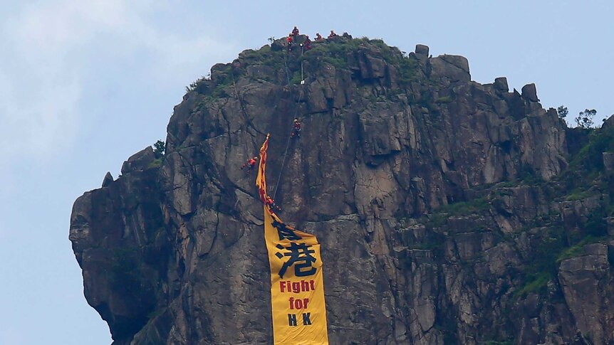 Firefighters remove a yellow banner with the words "Fight for Hong Kong" from Lion Rock mountain.