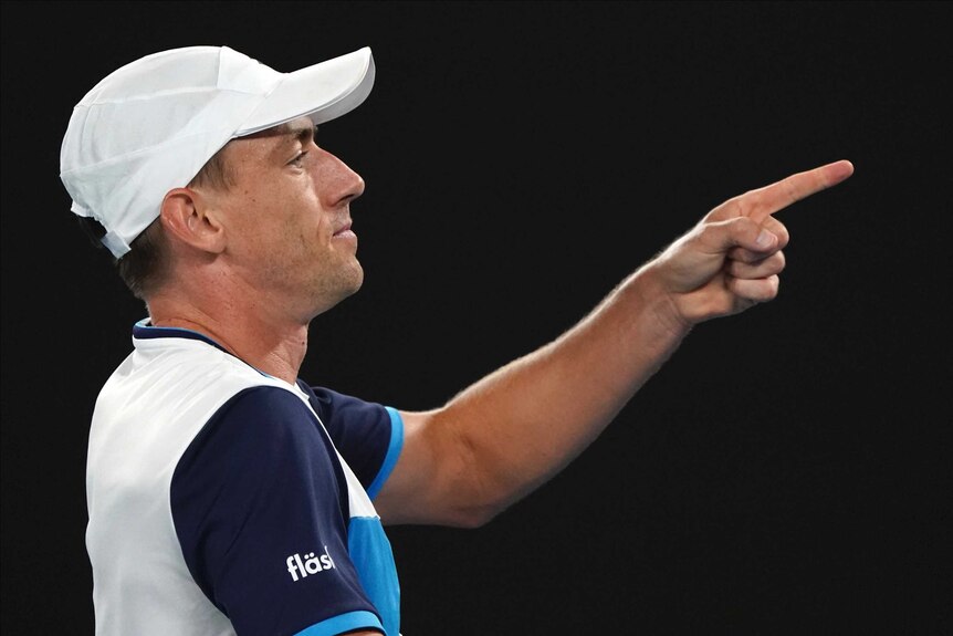 A males tennis player wearing a cap looks side on as he plays at the Australian Open.