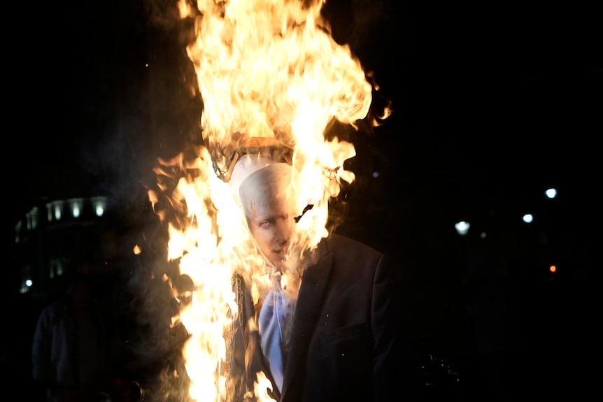 An effigy of Britain's Prime Minister Boris Johnson is set alight, with bright flames ascending into a dark night sky.