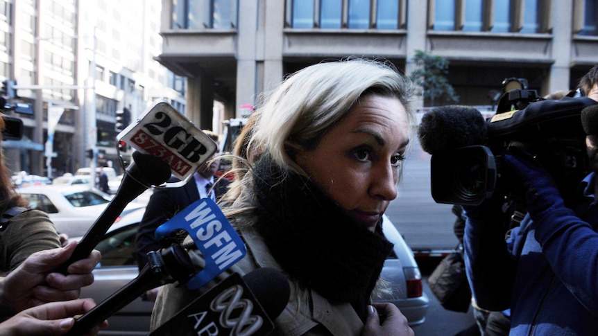 A blonde woman faces a press pack