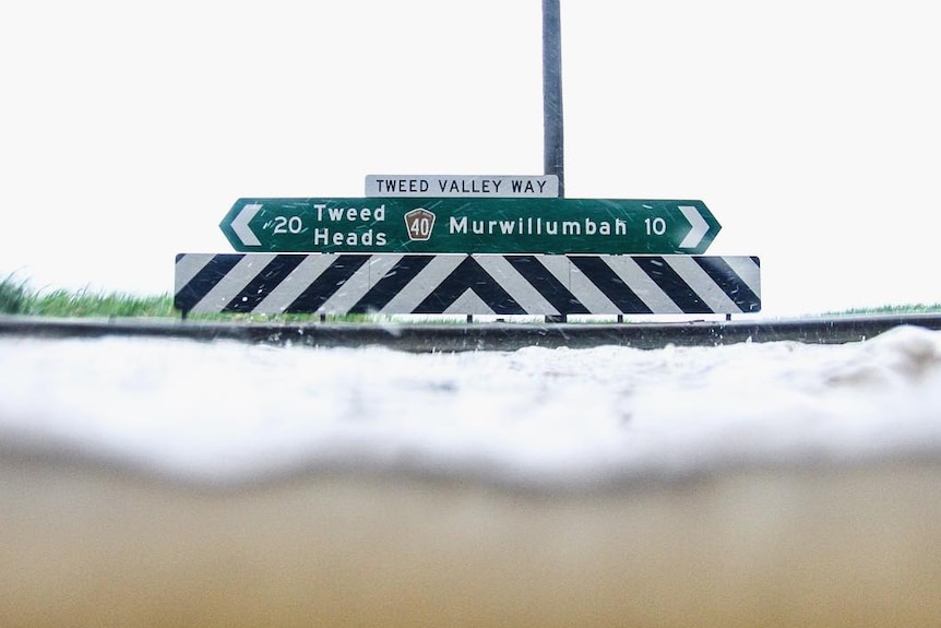 Water level reaches the guard rail at T-intersection road sign for Tweed Heads and Murwillumbah.