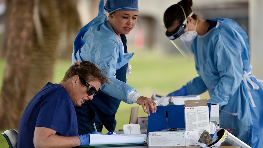 three female healthcare workers in full protective gear at an outside table