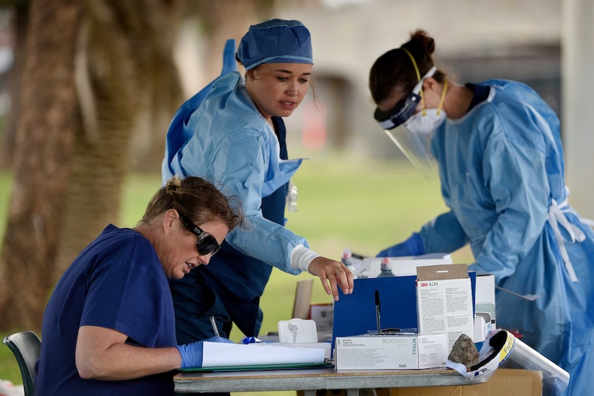 three female healthcare workers in full protective gear at an outside table