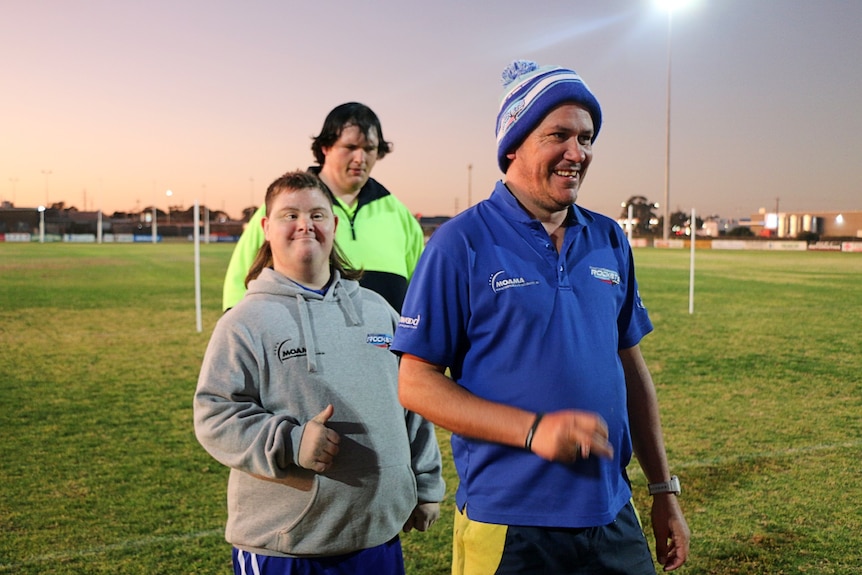 Peter is giving the thumbs up while waiting with other players on a footy oval.