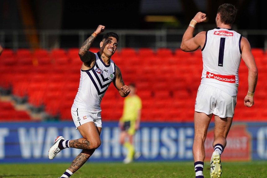 An AFL player runs back to a teammate with his fist in the air in celebration after kicking a goal.