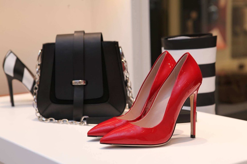 Shiny red leather stilettos and a black handbag on a shelf in a boutique.