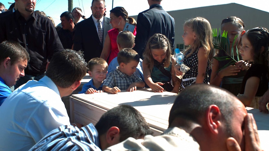 Kids with sombre faces surround a coffin at a funeral